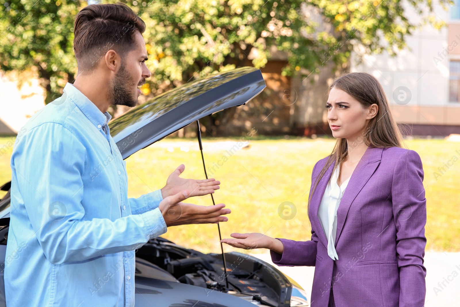 Photo of Couple arguing near broken car on city street