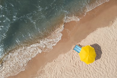Image of Yellow beach umbrella and sunbed on sandy coast near sea, aerial view. Space for text