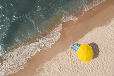 Yellow beach umbrella and sunbed on sandy coast near sea, aerial view. Space for text