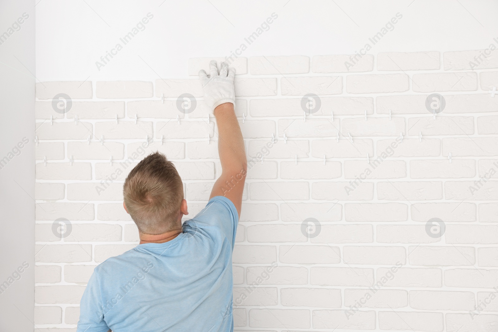 Photo of Professional builder installing new white decorative bricks on wall, back view