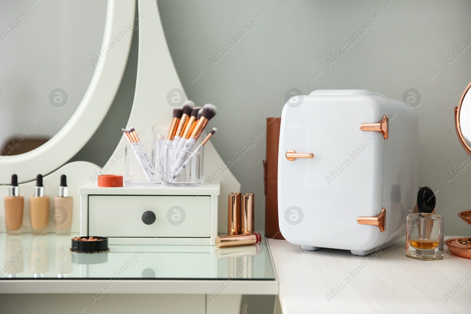 Photo of Cosmetics refrigerator and skin care products on white vanity table indoors