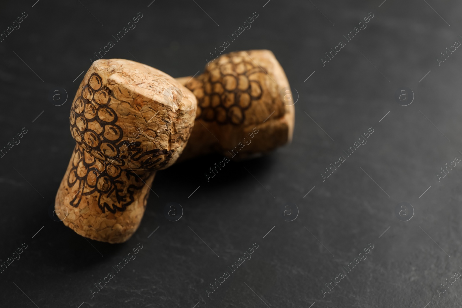 Photo of Sparkling wine corks with grape images on black table, closeup. Space for text