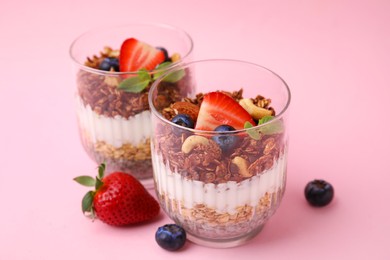 Photo of Tasty granola with berries, nuts, yogurt and chia seeds in glasses on pink background