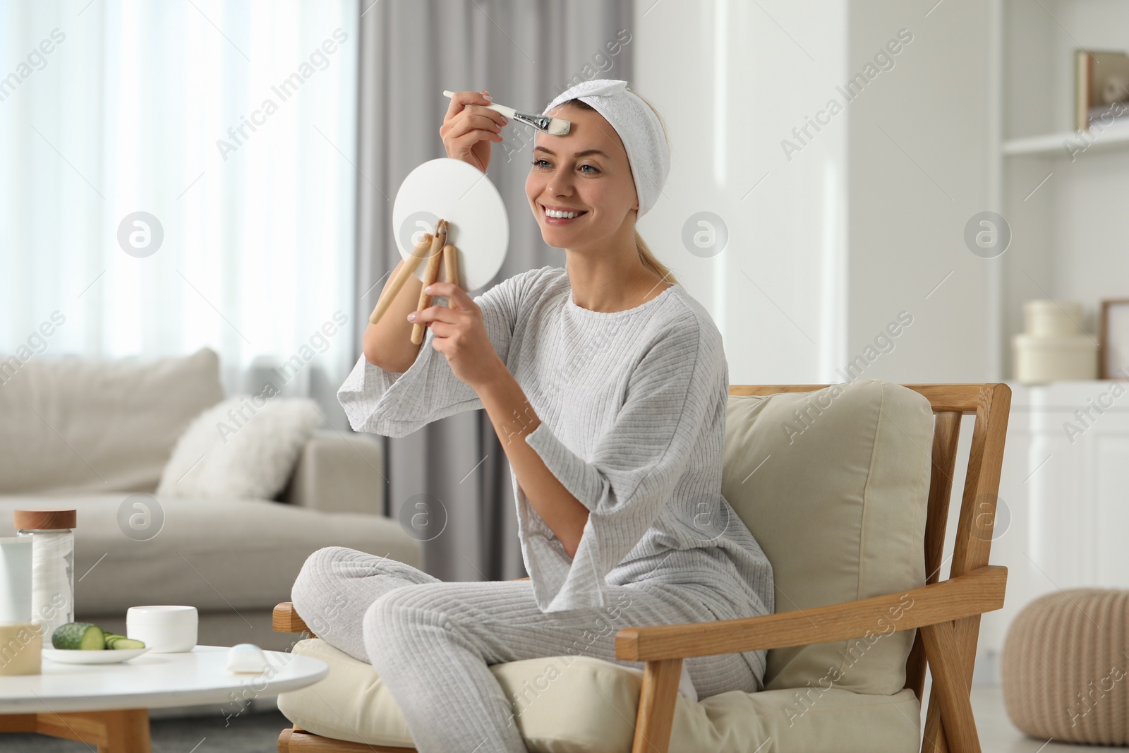 Photo of Young woman applying face mask in front of mirror at home. Spa treatments