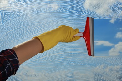Woman cleaning glass with squeegee indoors, closeup