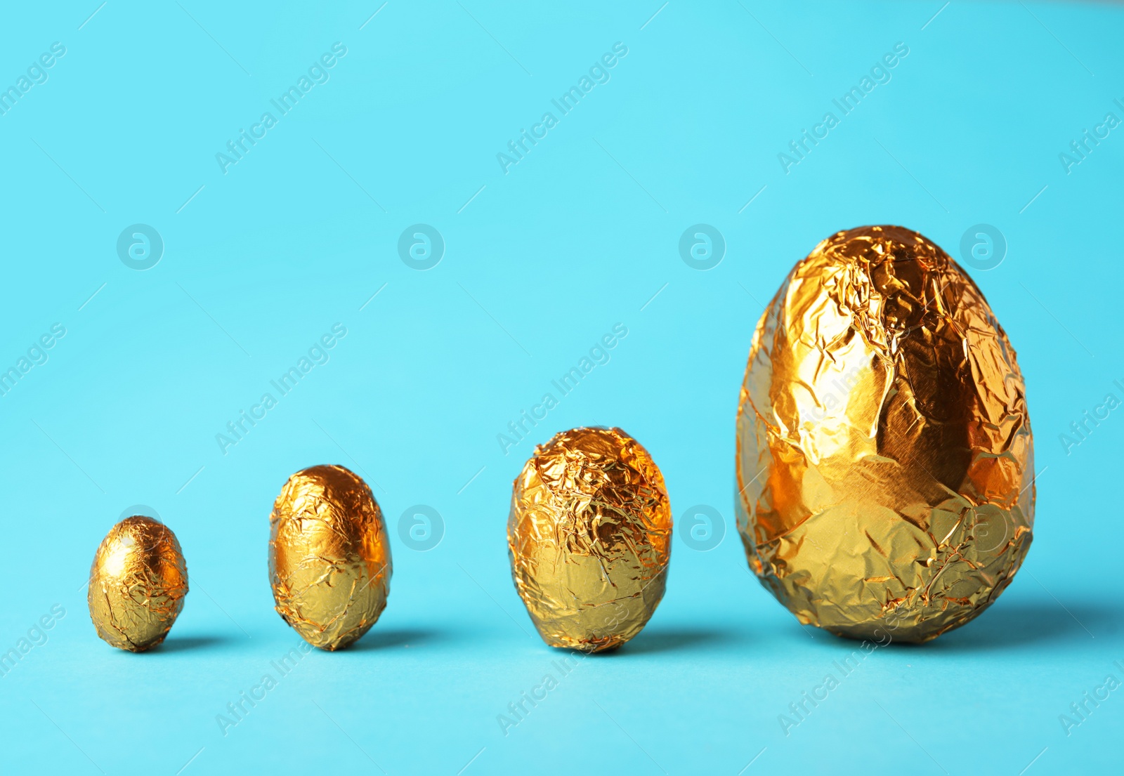 Photo of Chocolate eggs wrapped in golden foil on light blue background. Space for text