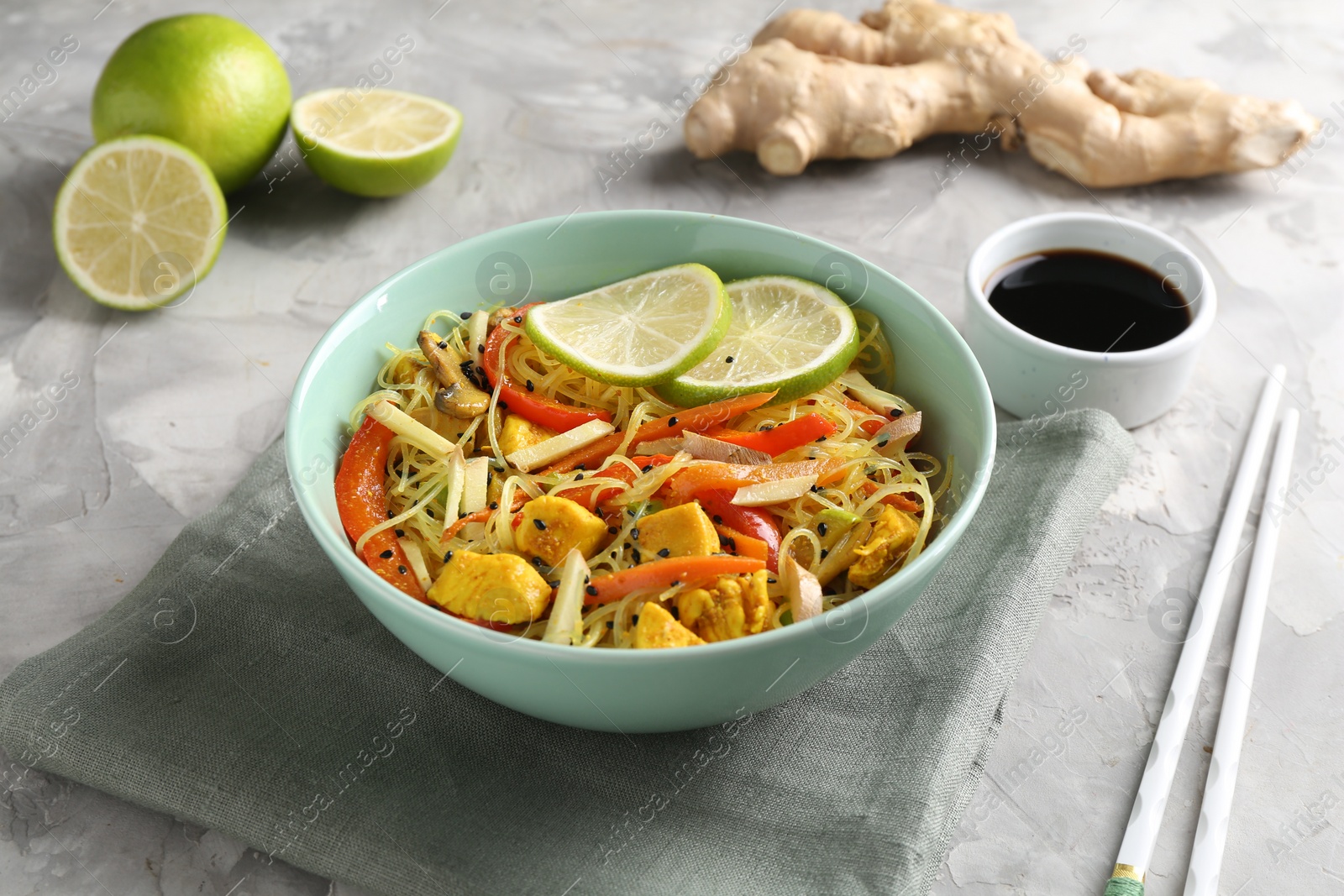 Photo of Stir-fry. Delicious cooked noodles with chicken and vegetables in bowl served on gray textured table