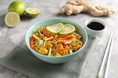 Photo of Stir-fry. Delicious cooked noodles with chicken and vegetables in bowl served on gray textured table