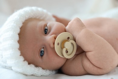 Cute newborn baby in white knitted hat lying on bed, closeup