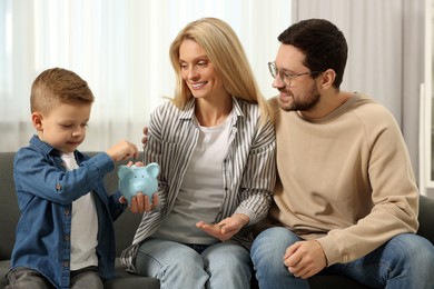 Photo of Family budget. Little boy putting coin into piggy bank and his parents at home