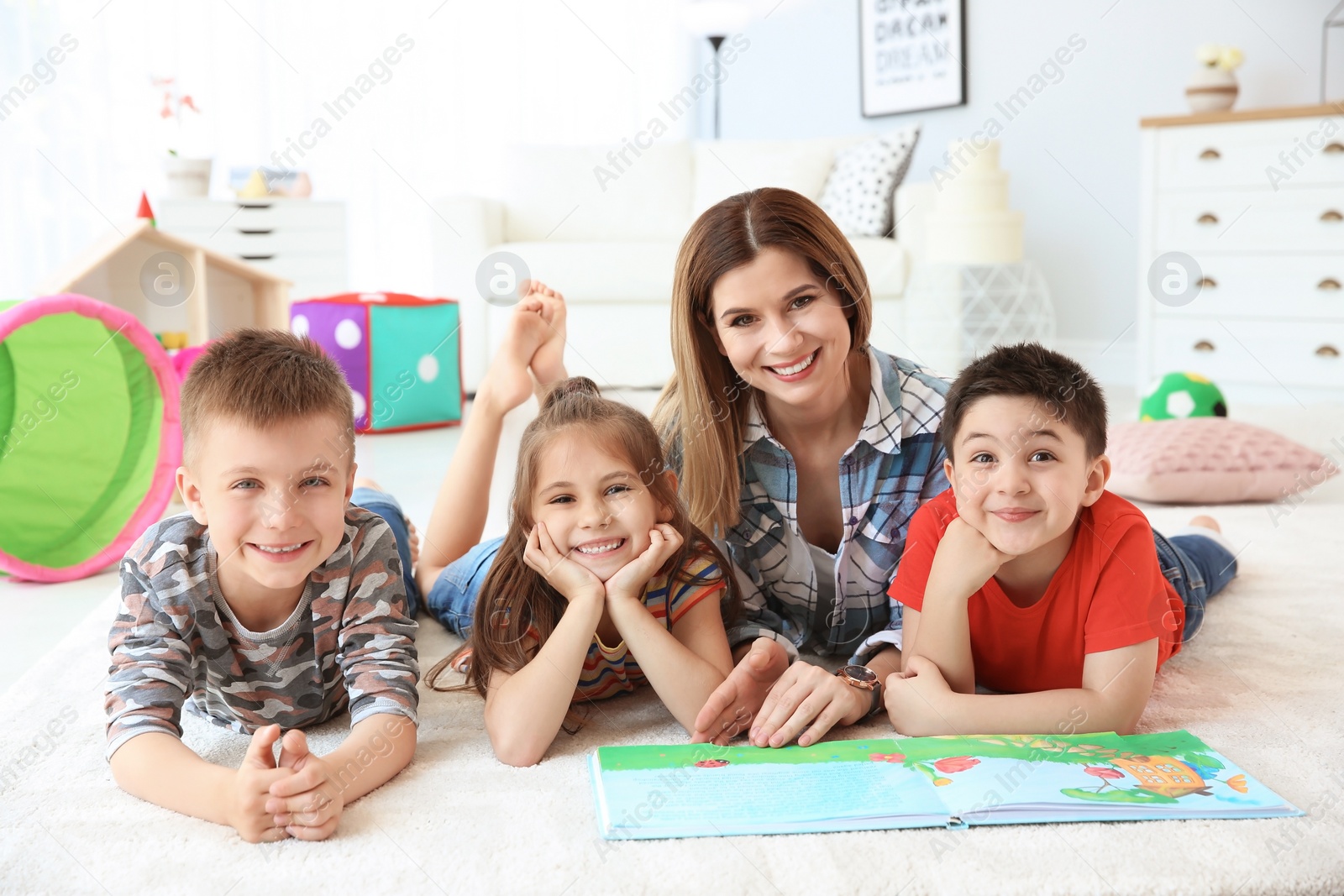 Photo of Cute little children reading book on floor with young mother in playing room