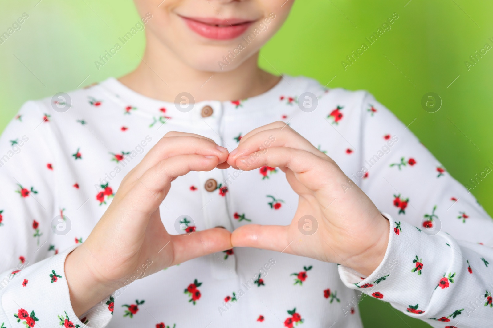 Photo of Little girl making heart with hands on blurred background, closeup