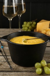 Fondue pot with melted cheese, glasses of wine and different products on wooden table