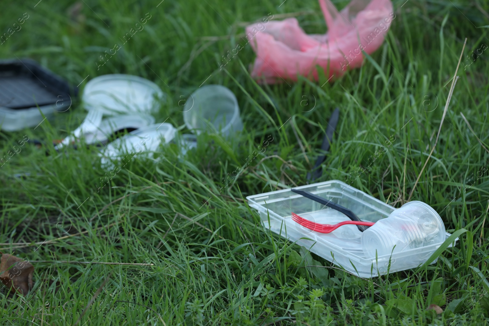 Photo of Used plastic tableware on grass outdoors, closeup. Environmental pollution concept