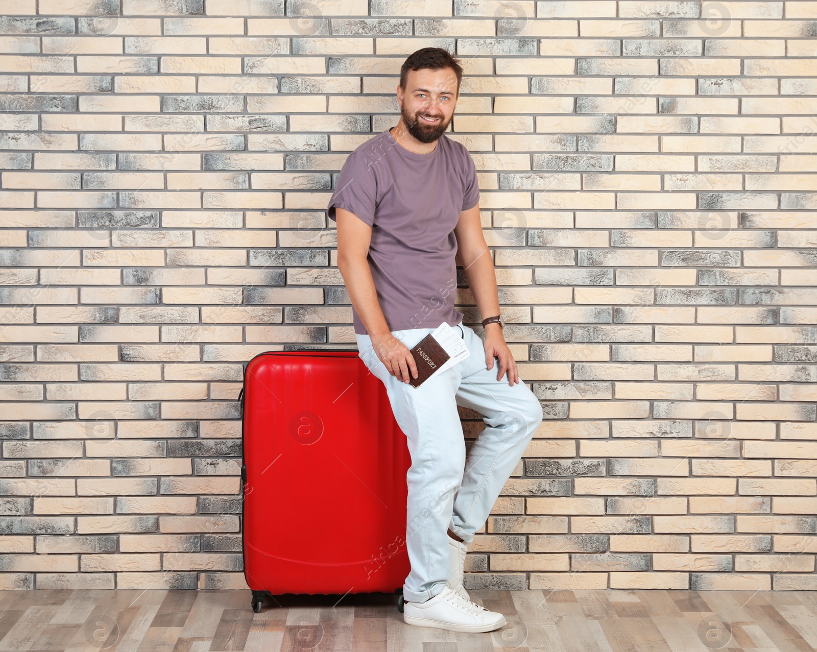 Photo of Man with suitcase and passport near brick wall. Vacation travel