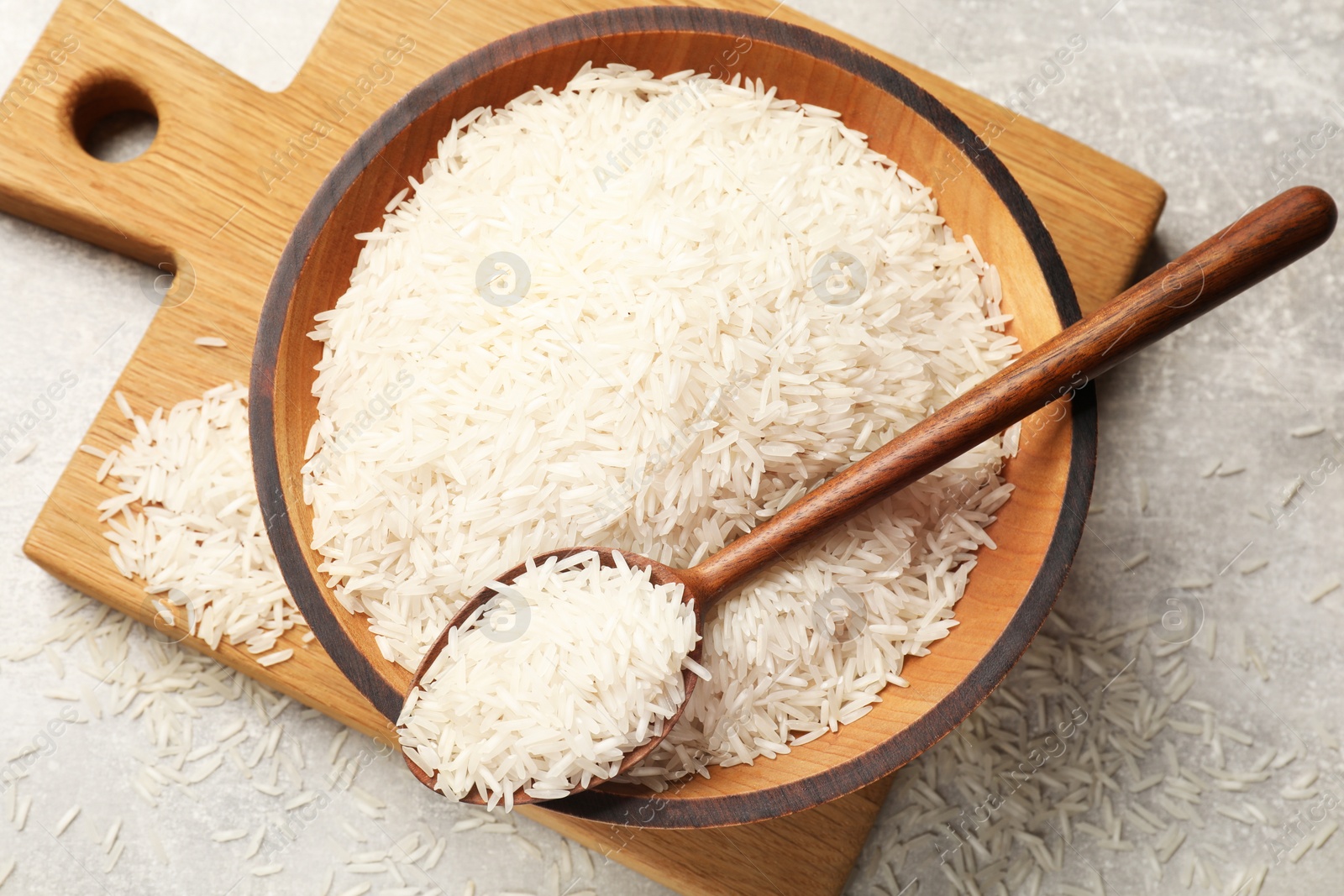 Photo of Raw basmati rice in bowl and spoon on grey table, top view