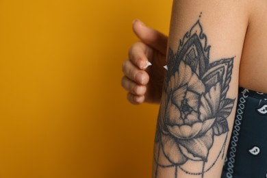 Photo of Woman applying cream onto her arm with tattoo on yellow background, closeup. Space for text