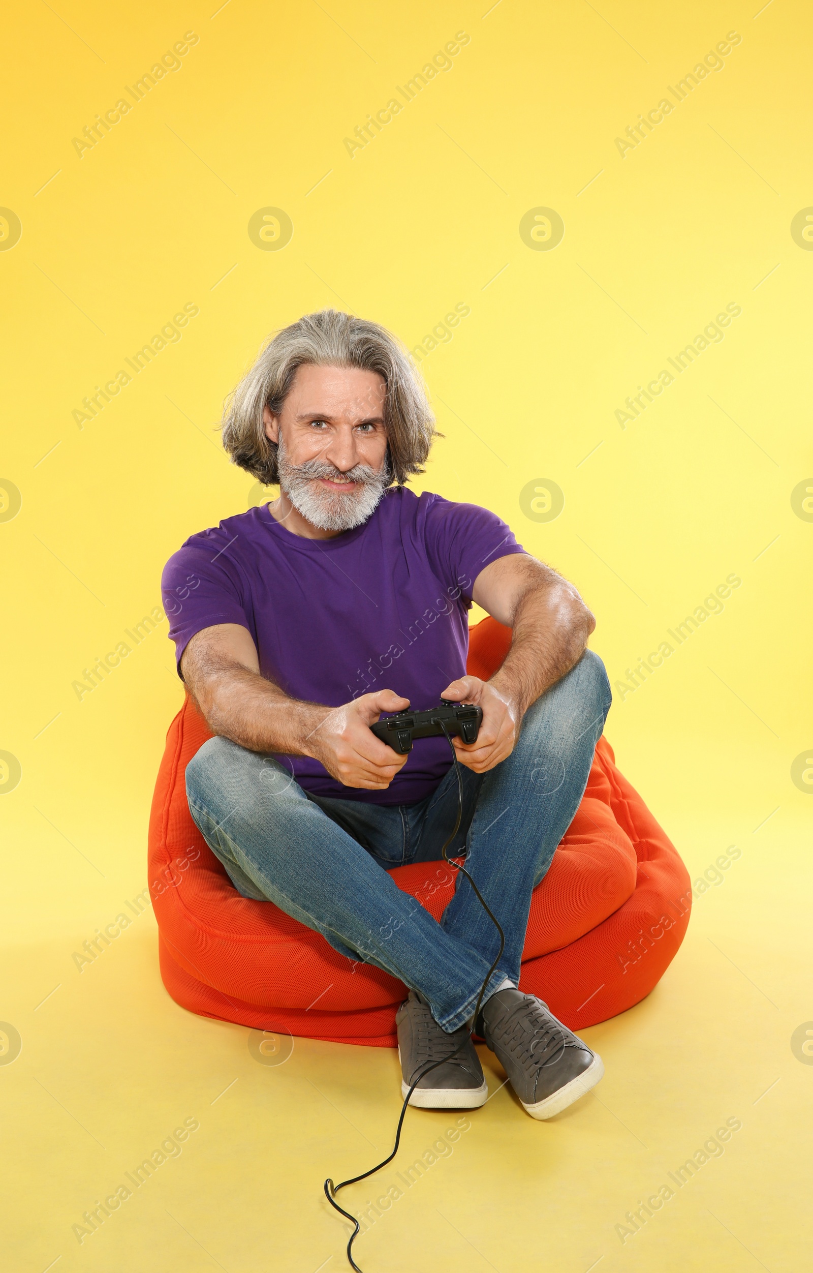 Photo of Emotional mature man playing video games with controller on color background