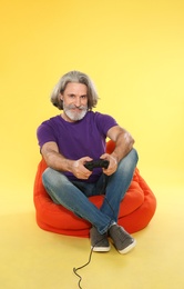 Photo of Emotional mature man playing video games with controller on color background