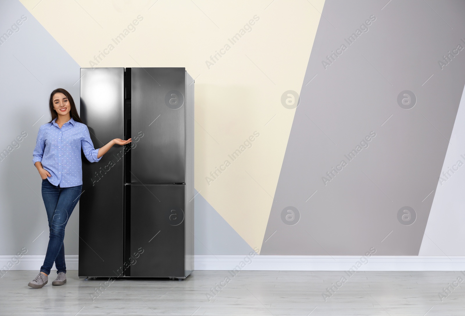 Photo of Happy young woman near refrigerator indoors, space for text