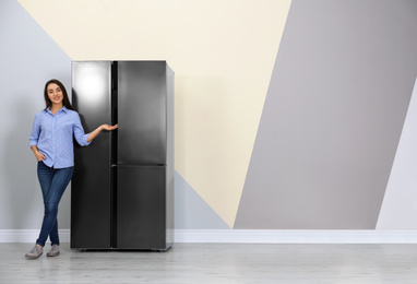 Happy young woman near refrigerator indoors, space for text