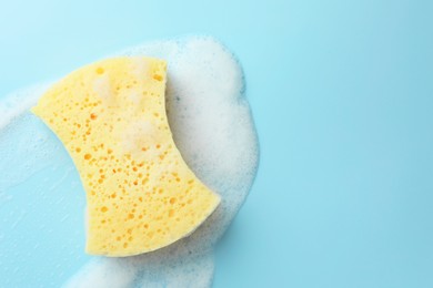 Yellow sponge with foam on light blue background, top view. Space for text