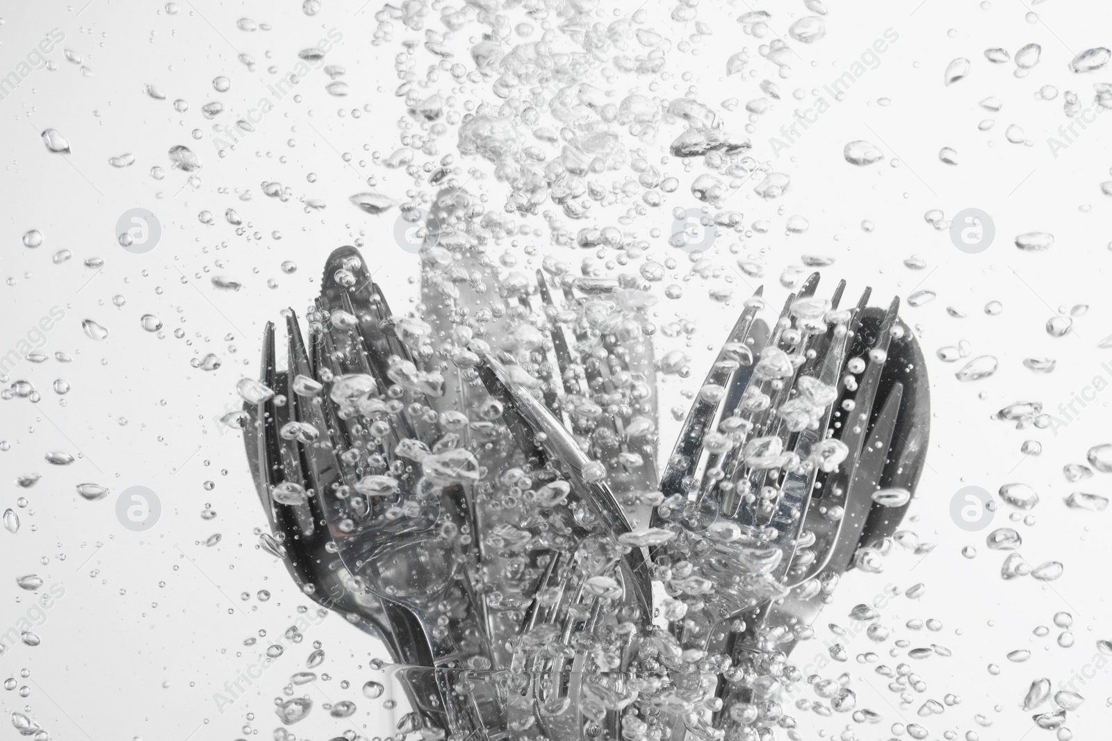 Photo of Washing silver cutlery in water on white background