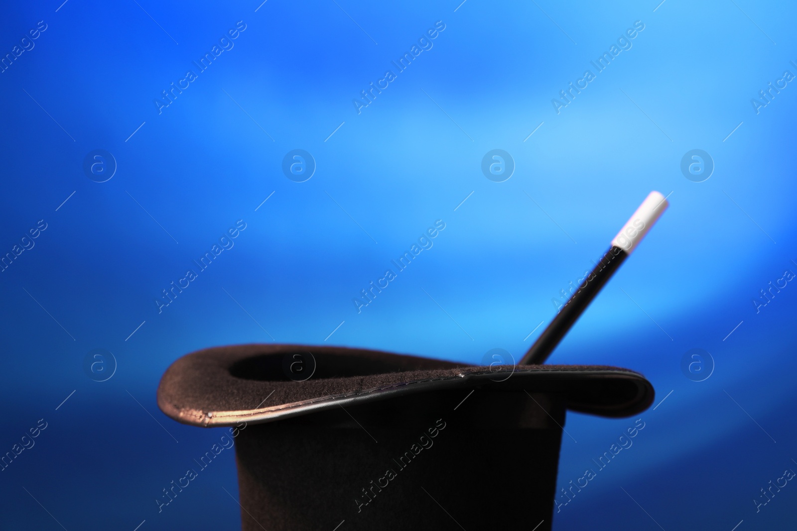 Photo of Magician's hat and wand on blue background, space for text