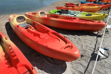 Many bright kayaks on sand near river