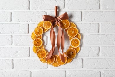 Photo of Decorative wreath made with dry oranges and ribbon hanging on white brick wall
