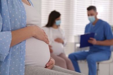 Pregnant woman waiting for appointment while doctor consulting other patient in clinic, focus on belly