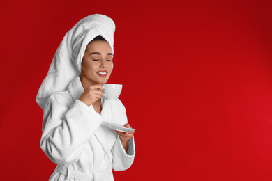 Photo of Young woman in bathrobe with cup of coffee on red background. Space for text