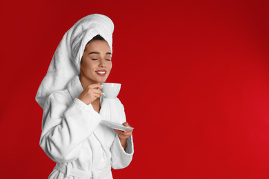 Young woman in bathrobe with cup of coffee on red background. Space for text