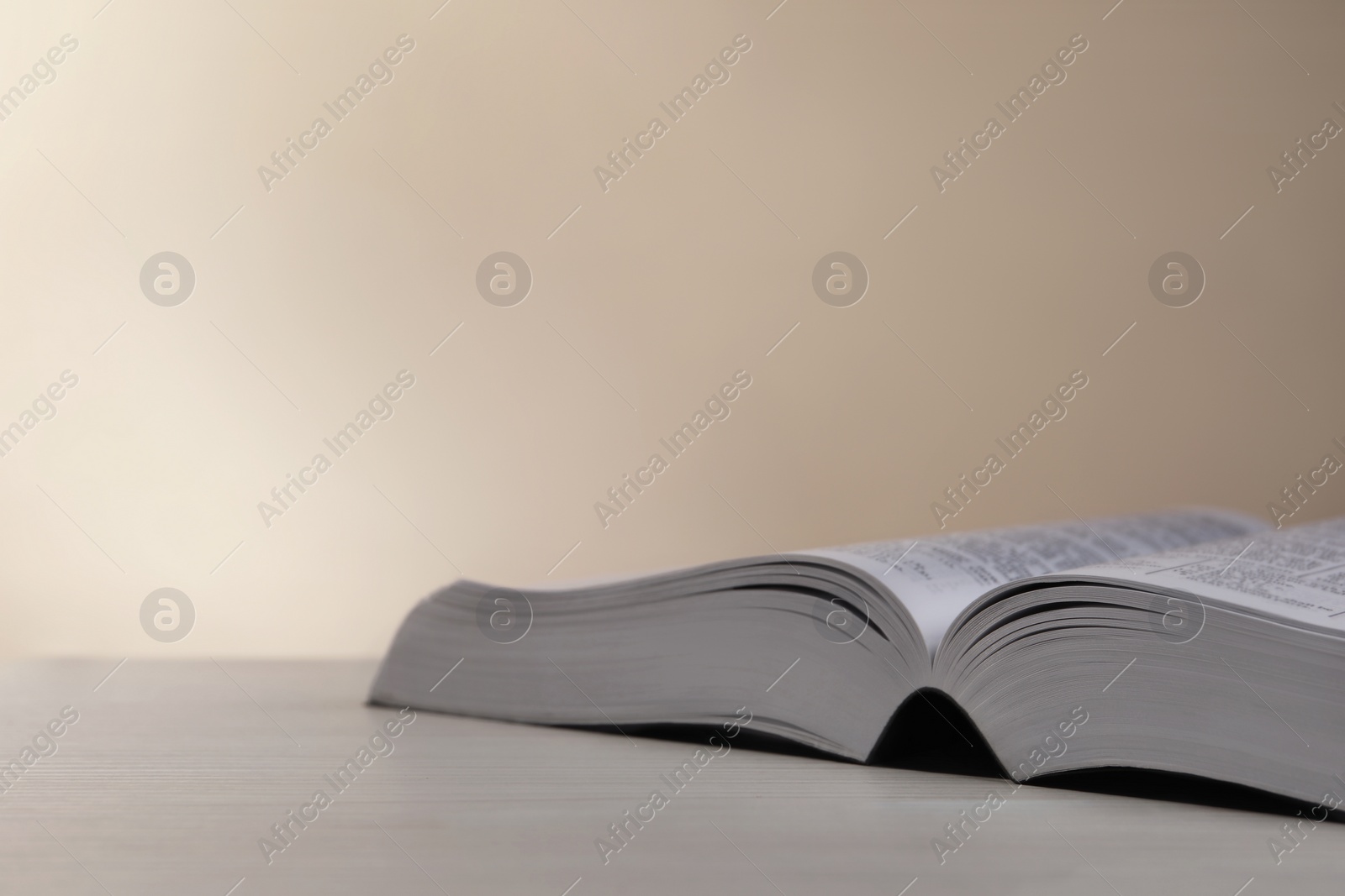 Photo of Open Bible on white wooden table against beige background. Space for text