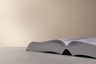 Open Bible on white wooden table against beige background. Space for text