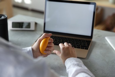 Woman squeezing antistress ball while working on laptop in office, closeup