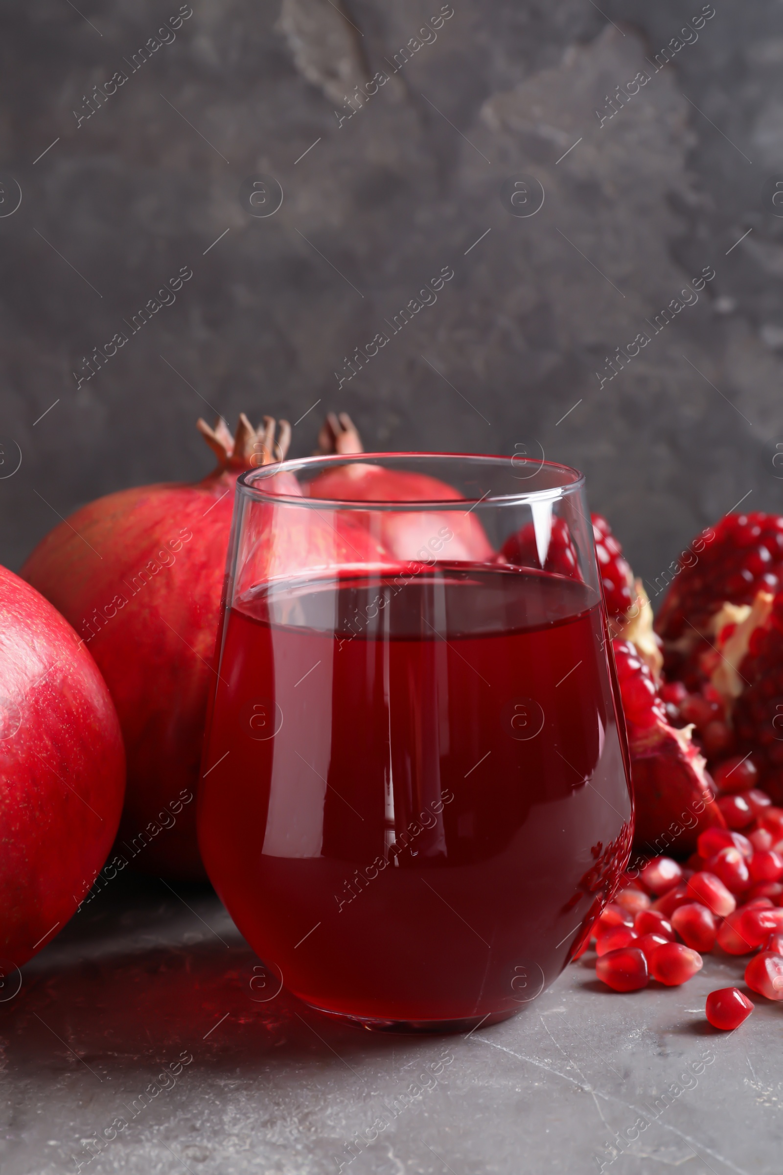 Photo of Glass of pomegranate juice and fresh fruits on table against grey background