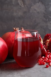 Photo of Glass of pomegranate juice and fresh fruits on table against grey background