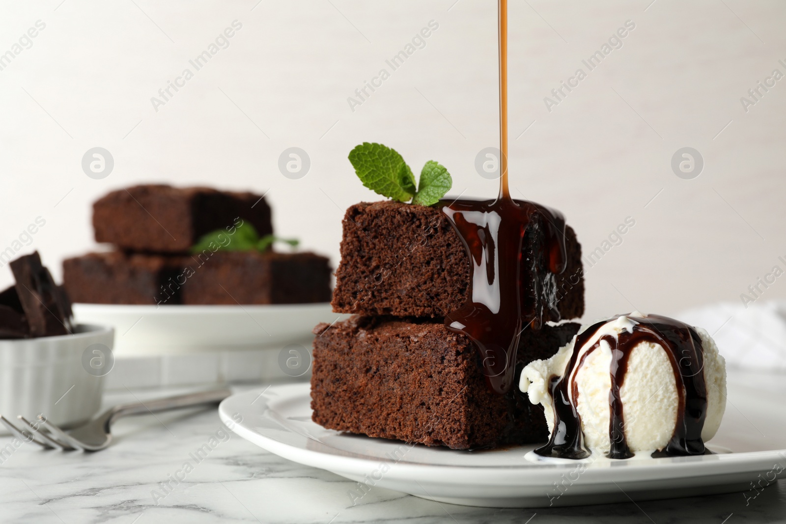 Photo of Pouring sauce onto fresh brownies served with ice-cream on plate, space for text. Delicious chocolate pie