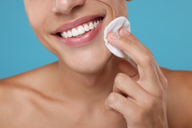 Photo of Man cleaning face with cotton pad on light blue background, closeup