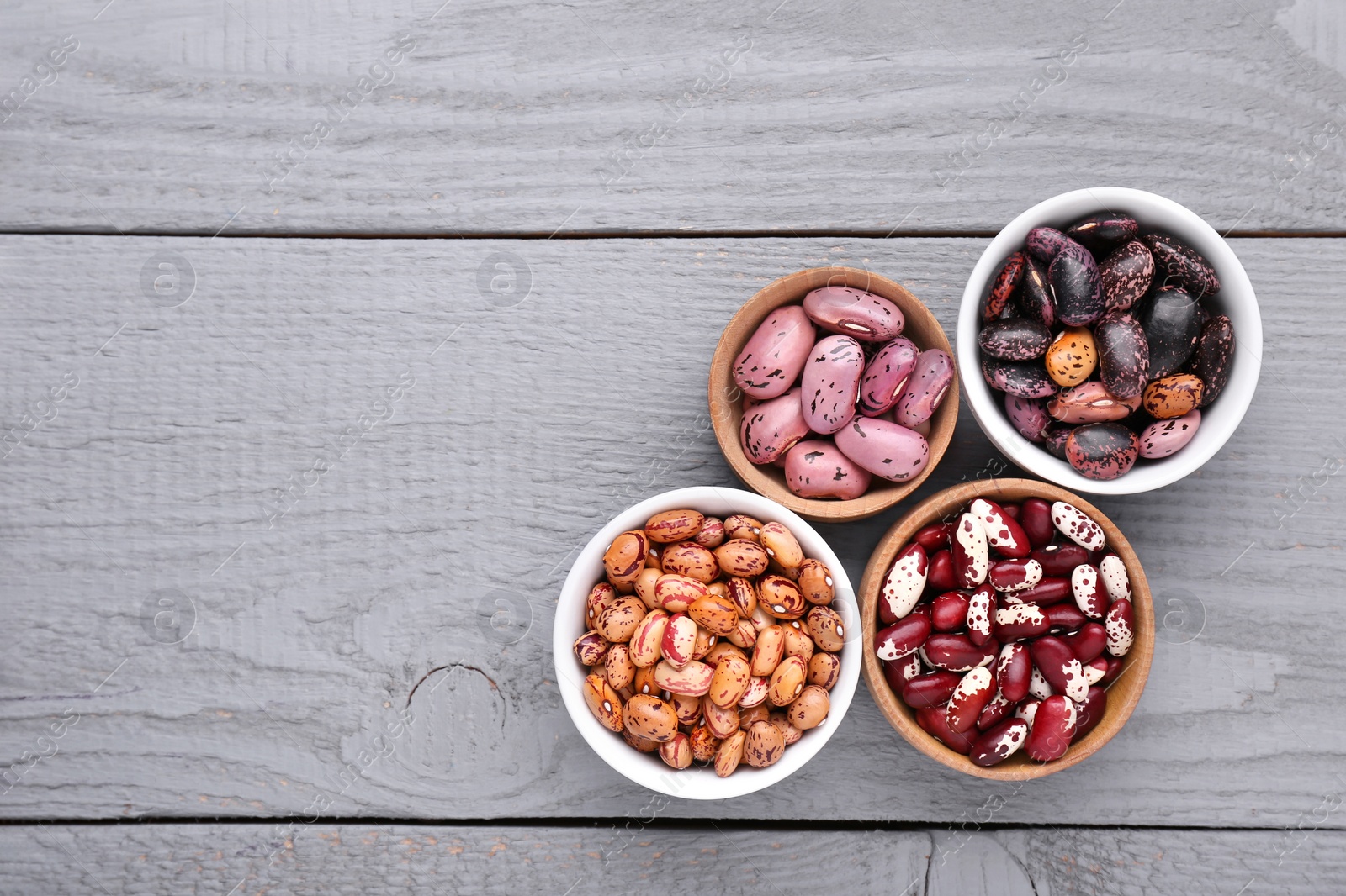 Photo of Different kinds of dry kidney beans on grey wooden table, flat lay. Space for text