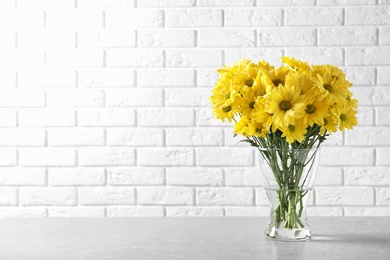 Photo of Vase with beautiful chamomile flowers on table against brick wall. Space for text