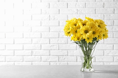 Vase with beautiful chamomile flowers on table against brick wall. Space for text