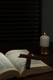 Cross, Bible and church candle on wooden table, space for text