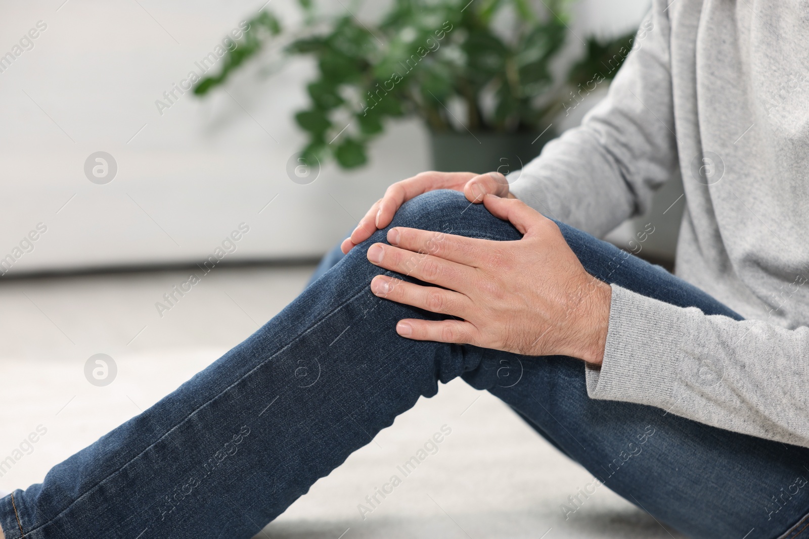 Photo of Man suffering from leg pain on white carpet indoors, closeup