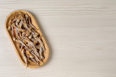 Photo of Plate of tasty dried anchovies on light wooden table, top view. Space for text