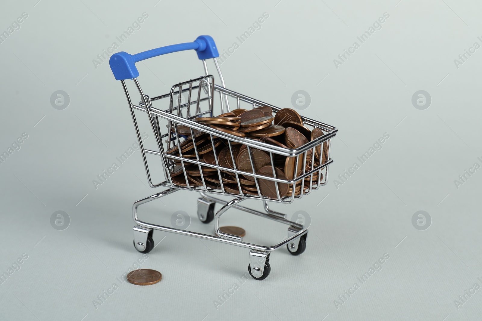 Photo of Small metal shopping cart with coins on light background