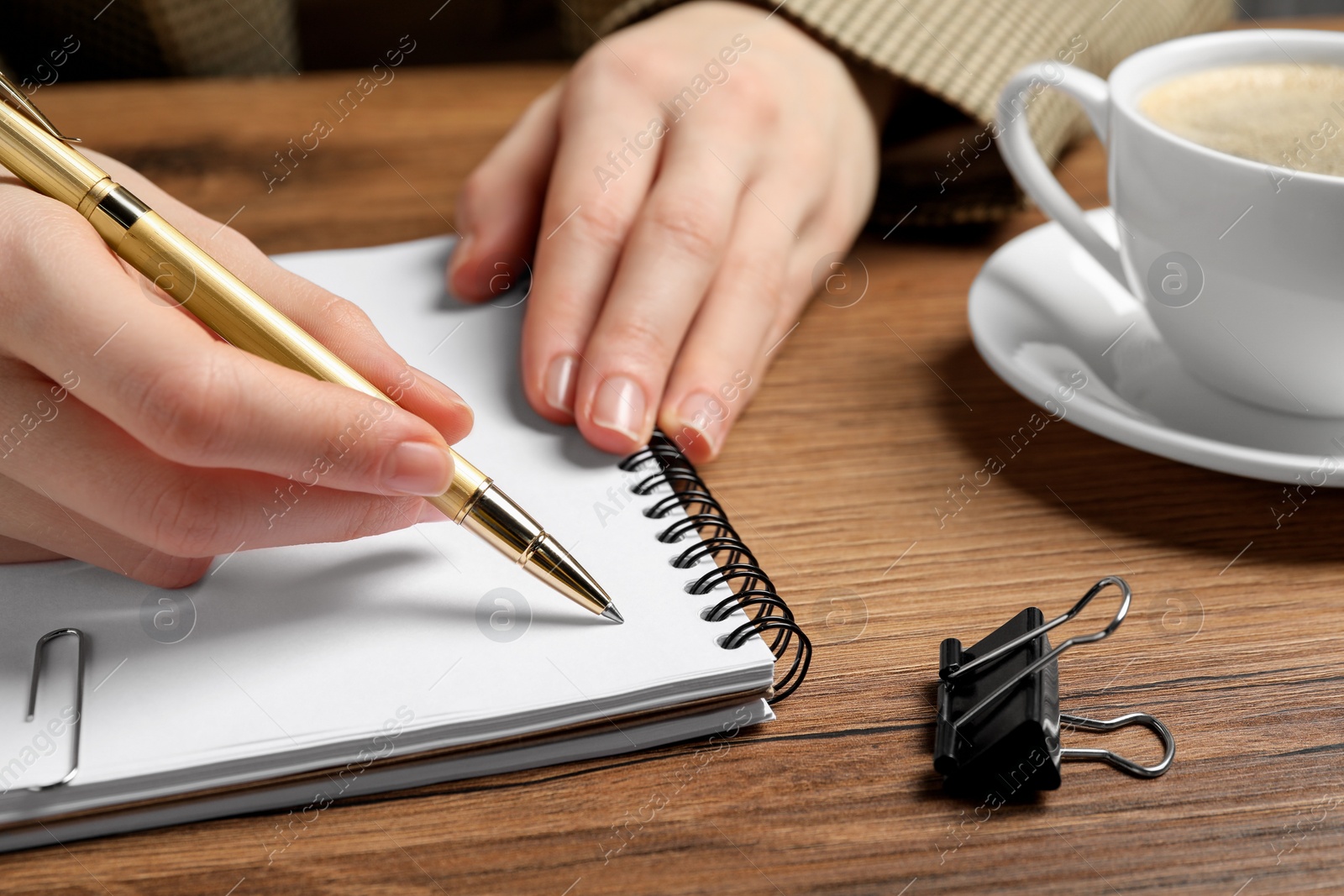 Photo of Woman writing in notebook at wooden table, closeup