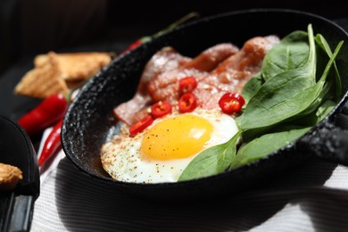 Photo of Tasty fried egg with bacon, chili pepper and spinach in pan, closeup