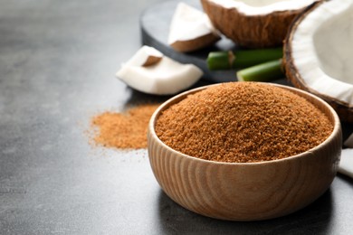 Natural coconut sugar in wooden bowl on grey table, space for text